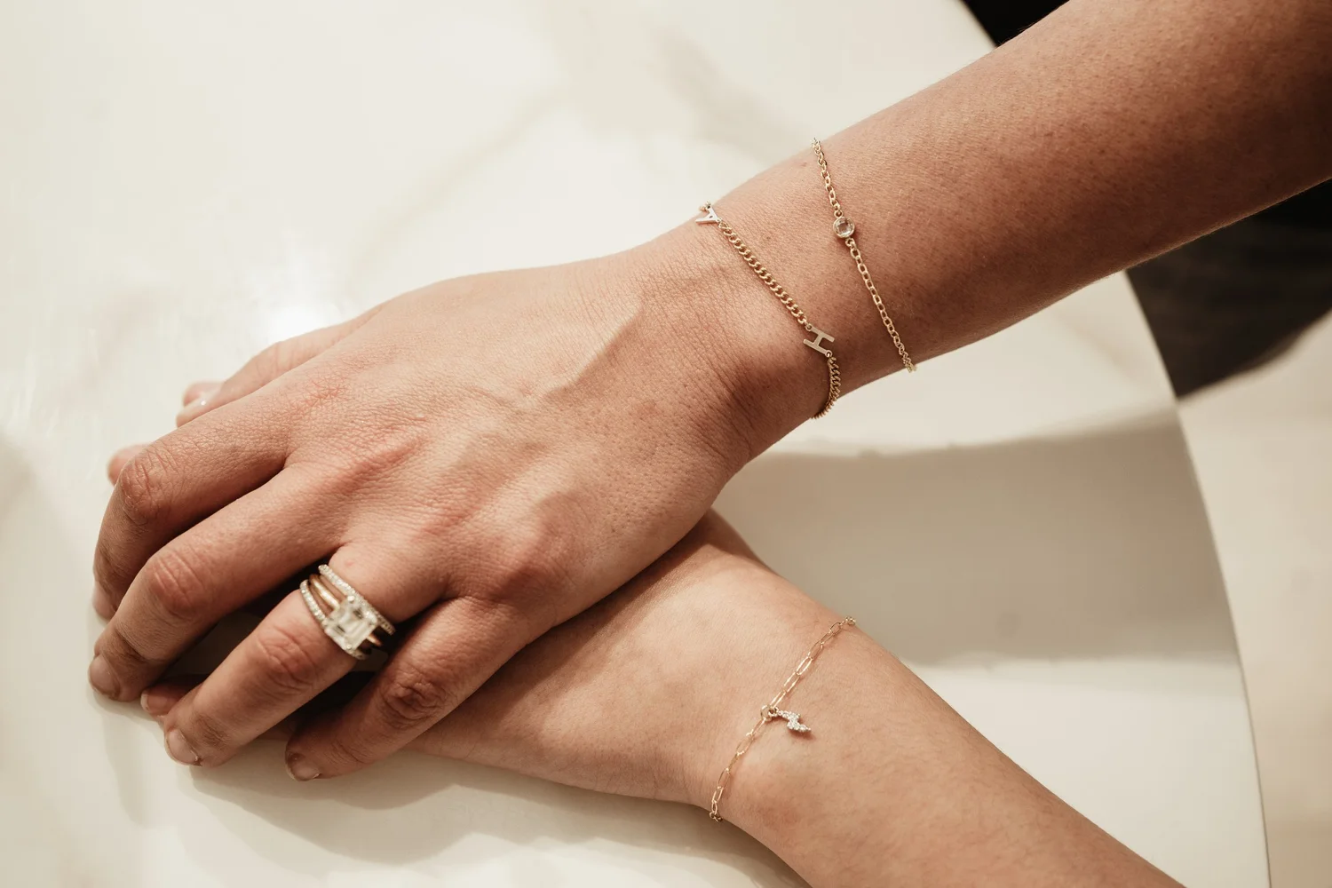 Close-up of two hands with delicate jewelry including bracelets, rings, and rings featuring a large central stone.