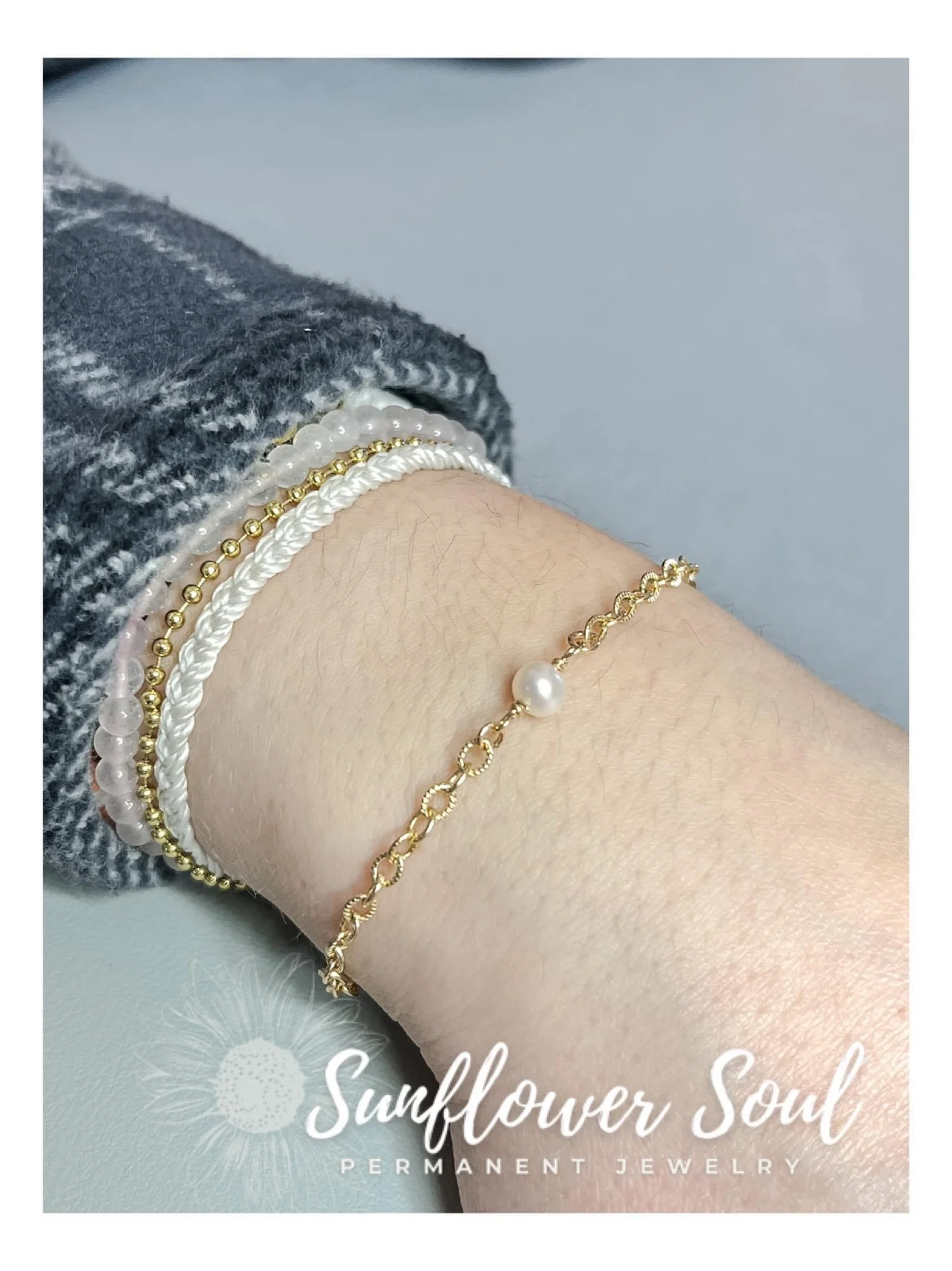Close-up of a wrist with multiple bracelets, including pearl, gold, and beaded strands, against a gray background and gray sweater.