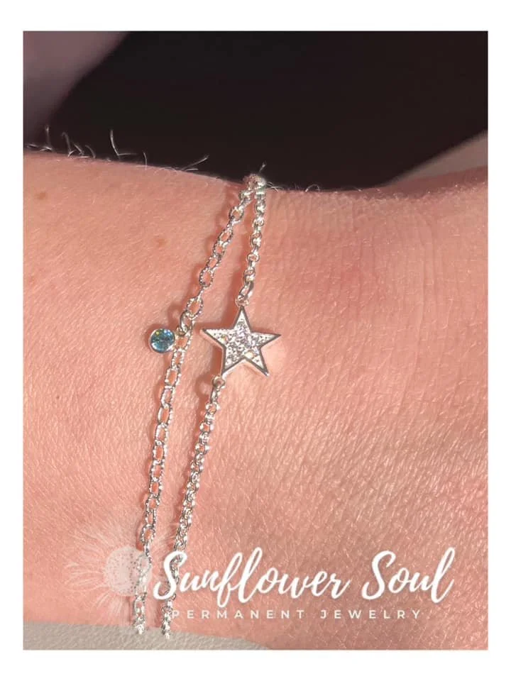 Silver anklet with a star-shaped charm and a small round gemstone on a person's ankle.