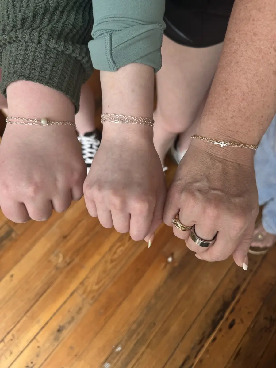 A close-up of four clenched fists with various jewelry and clothing, over a polished wooden floor.