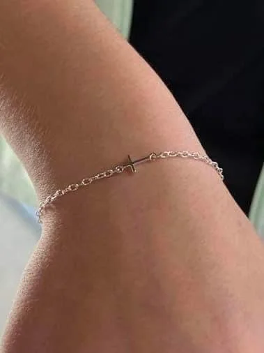 Close-up of a person's wrist with a delicate silver bracelet featuring a small cross charm.