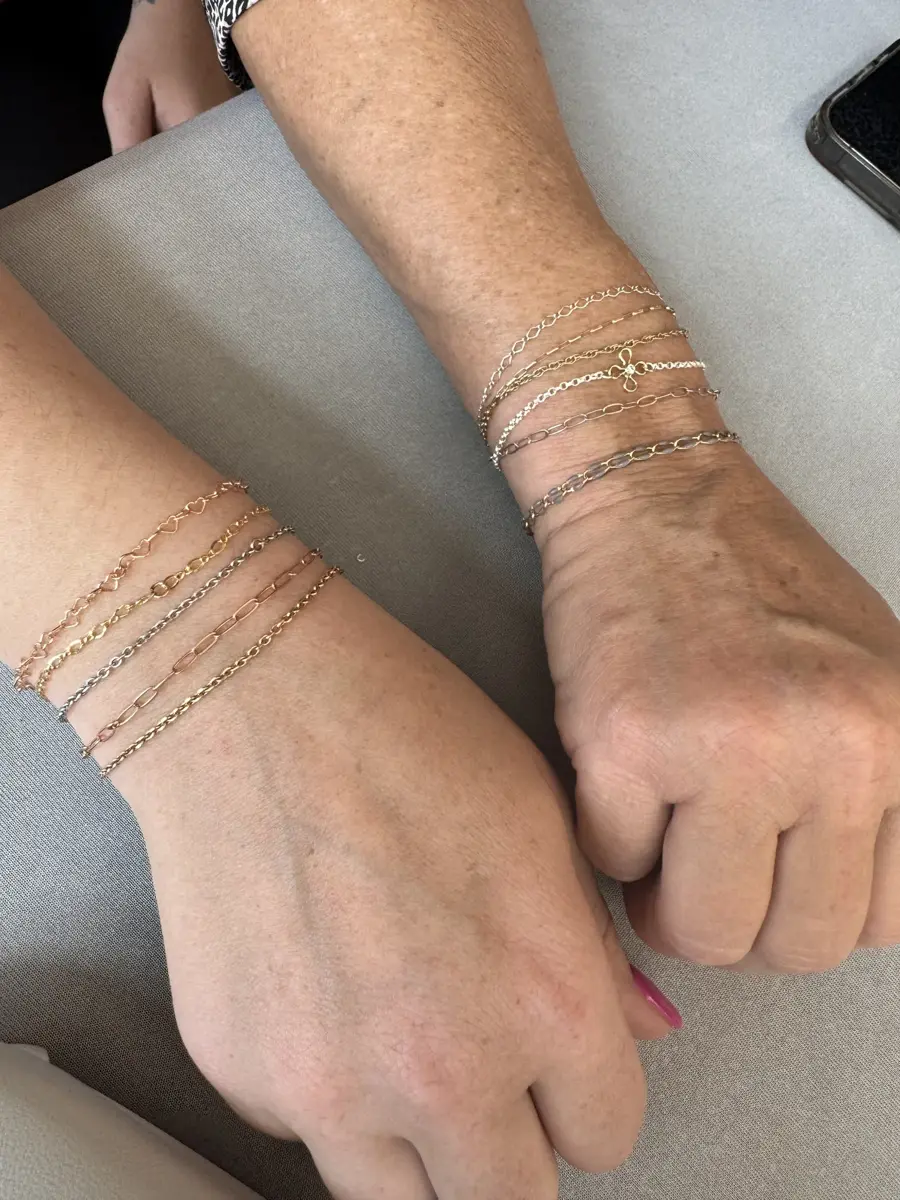 Close-up of two hands resting on a gray surface, showcasing various gold and silver chain bracelets.