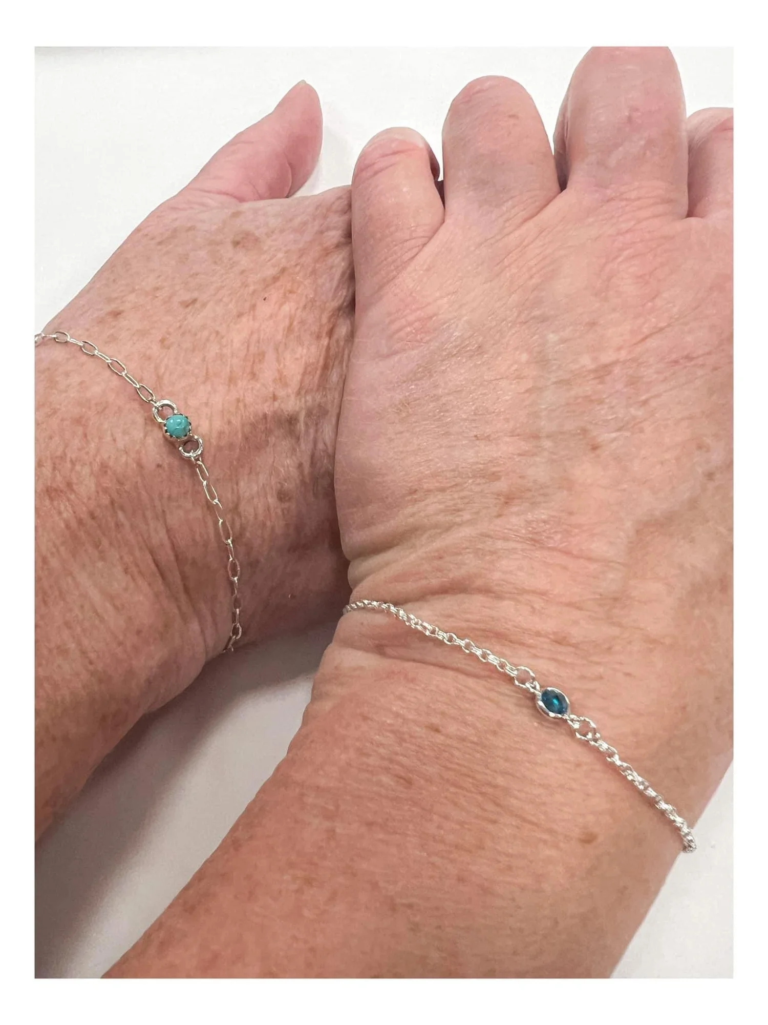 Close-up of two hands with matching silver bracelets with blue gemstones.