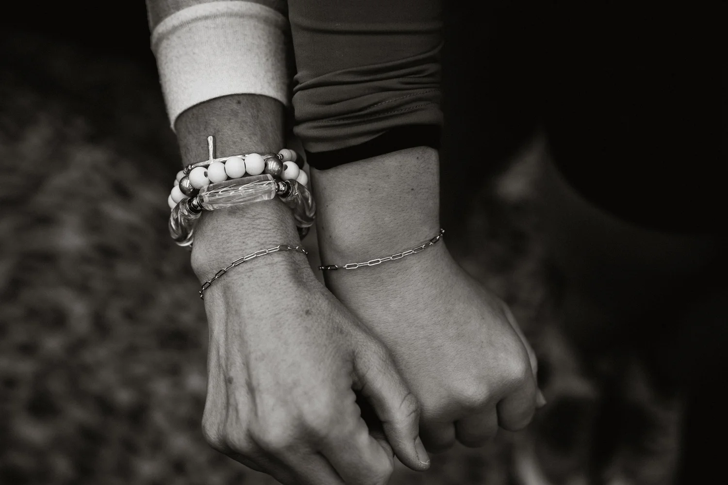 Close-up of two hands with bracelets, one hand holding the other, in black and white.