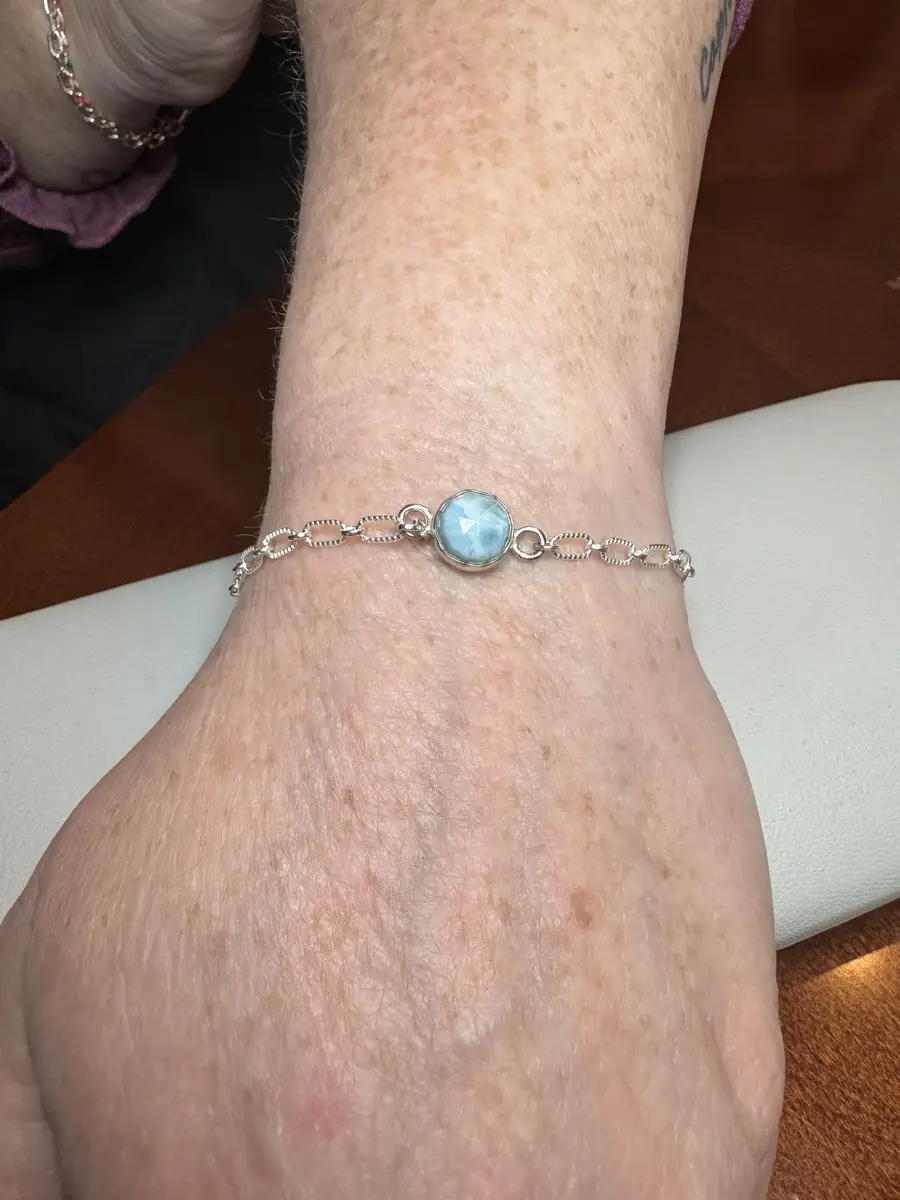 A close-up of a person's ankle wearing a silver bracelet with a blue gemstone.